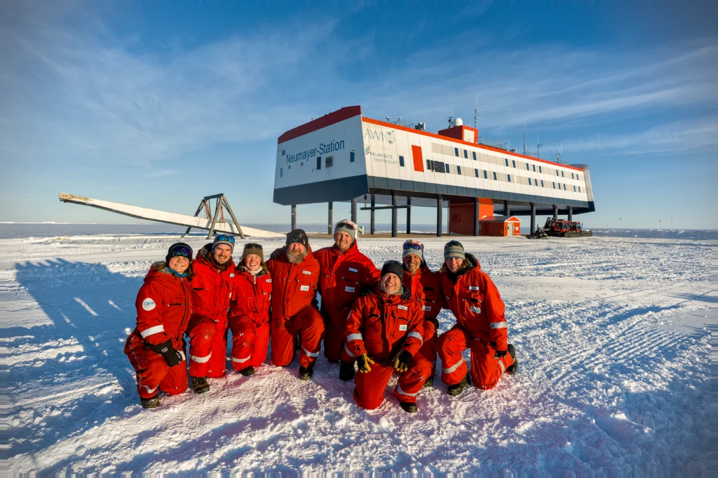 ÜWIS_cite_Lea_Buse Das Team vor der Neumayer-Station. Es ist sonnig und sie tragen rote Anzüge gegen die Kälte.