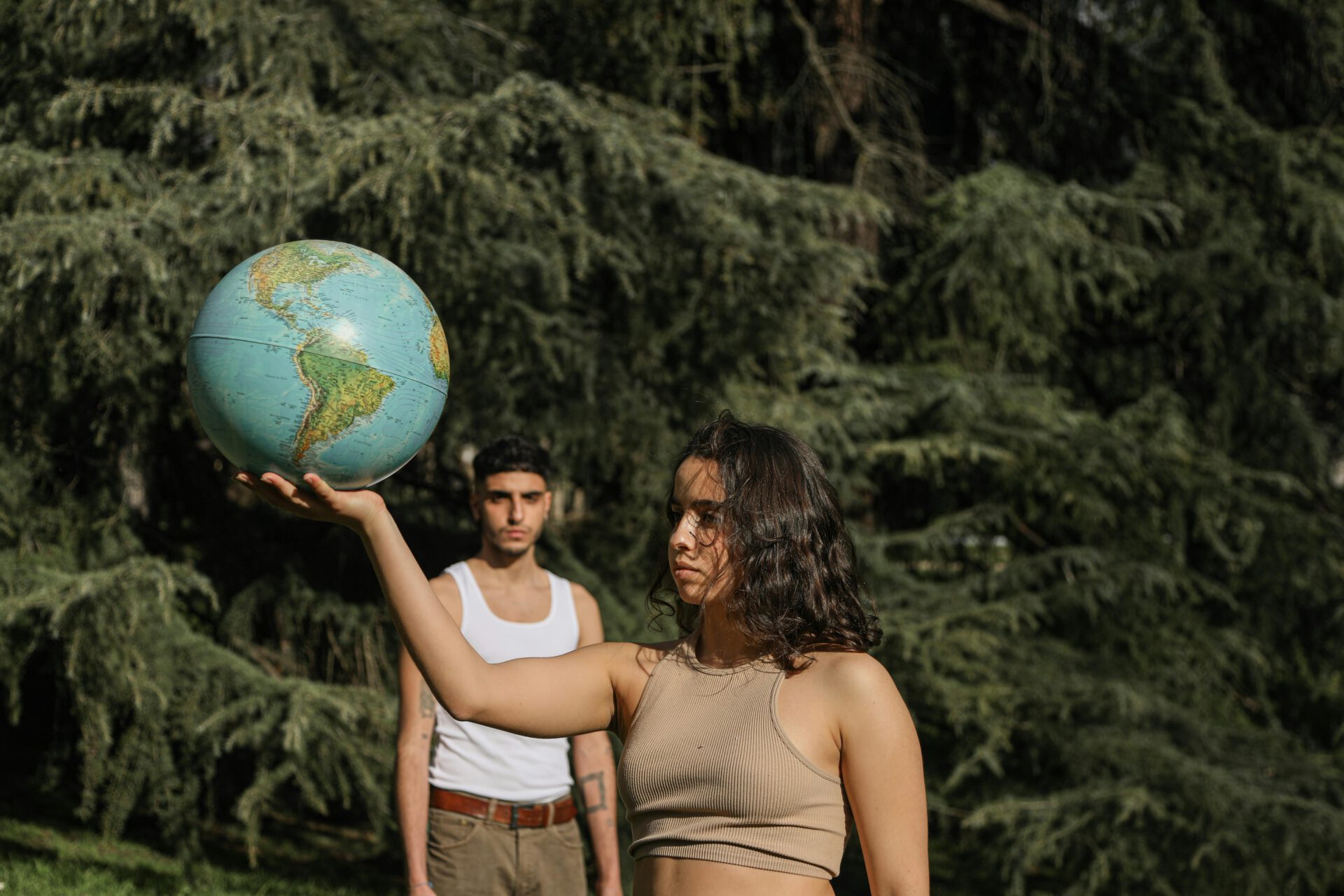 Two young adults hold a globe amidst lush greenery, symbolizing global awareness.