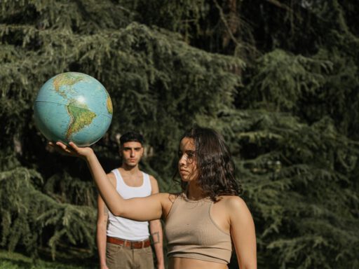Two young adults hold a globe amidst lush greenery, symbolizing global awareness.